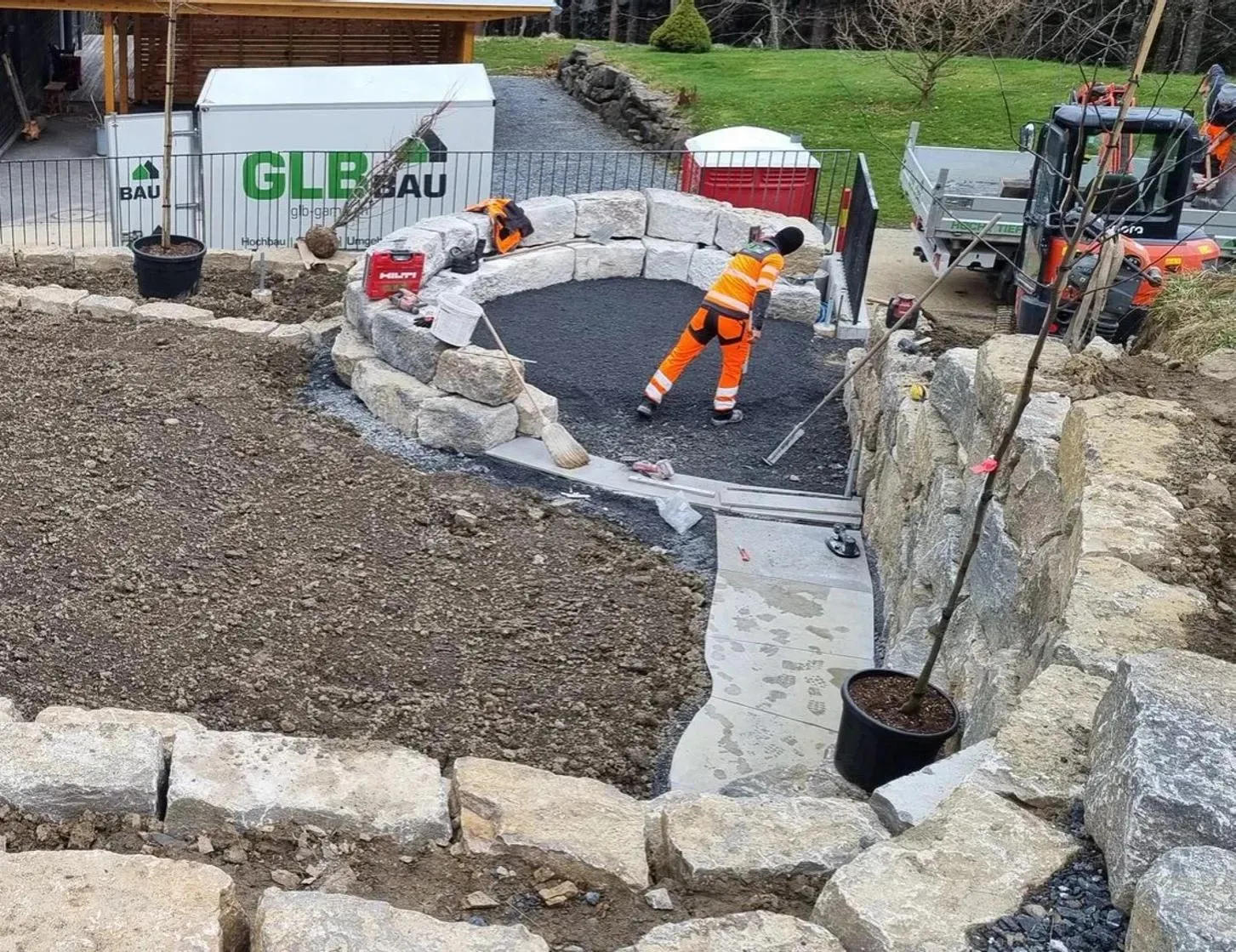 Mitarbeitende von GLB setzen auf einer Baustelle eine Gartenmauer aus Stein, dahinter ein Baustellencontainer von GLB Bau